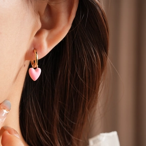 Close-up of a pink heart pendant with a gold hoop earring worn on a model's ear