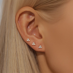 Close-up of three gold clover stud earrings with clear zircons on a female ear model