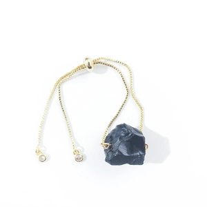 Detail of adjustable gold box chain bracelet with raw irregular black stone centerpiece