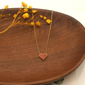Detail of red heart pendant with gold wavy border on a wooden tray with dried flowers