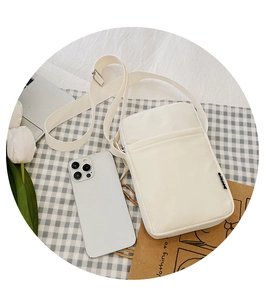 Flat lay of a white minimalist canvas crossbody phone bag on checkered fabric