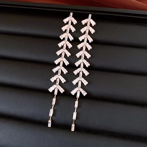 Macro shot of rose gold tassel earrings with leaf-shaped cubic zirconia on black leather