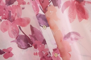 Dettaglio di camicia con stampa floreale rosa, tessuto setoso e bottoni rotondi