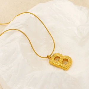 Macro shot of gold letter B pendant with lava texture on a minimalist white stone base