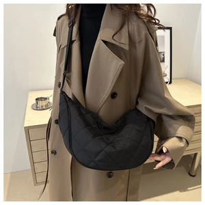 Close-up of black quilted nylon crescent bag worn with a casual trench coat
