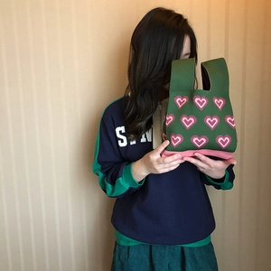 Knitted green tote bag with pink heart patterns held by a woman in casual style