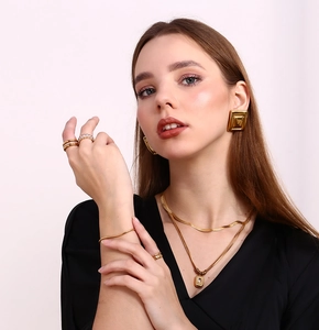 Detailed close-up of 18K gold plated geometric earrings and layered jewelry set on model