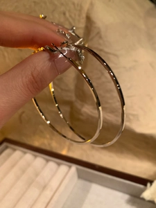 Close-up of hand holding minimalist polished silver oval hoop earrings in warm light