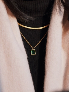 Close-up of a double-layered gold snake chain necklace with an emerald zircon pendant