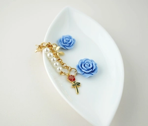 Detailed view of golden bracelet with red rose enamel charm and white faux pearls