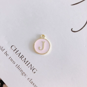 Macro shot of pink enamel round pendant with golden letter J for DIY jewelry making