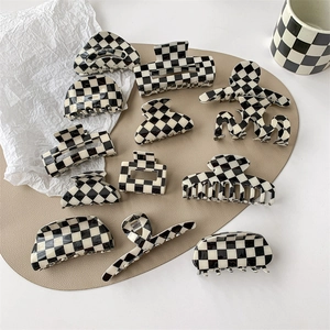 Collection of black and white checkerboard hair claws in various shapes on a beige mat