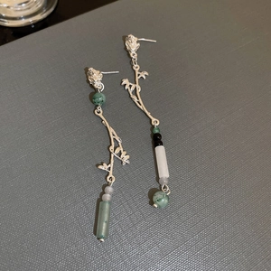Detail of silver branch earrings with emerald and grey beads on a textured grey background