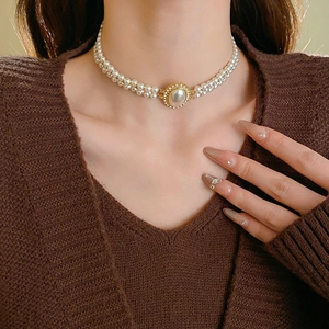 Close-up of double-layered pearl necklace with crystal-embedded golden pendant on neck