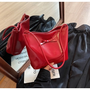 Detail view of red glossy shoulder bag with bow decoration and slim straps on mirror surface