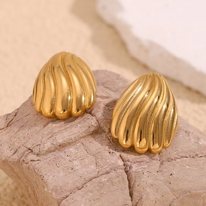 Gros plan de boucles d'oreilles coquillage dorées avec des rayures verticales sur pierre