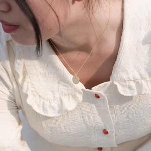 Detail of a gold coin necklace with a starburst pattern worn by a model in a close-up view