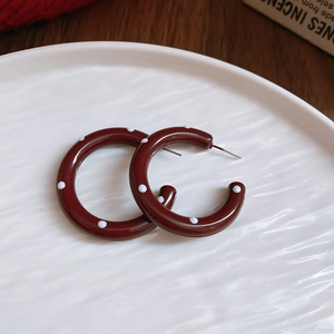 Macro shot of red C-shaped strawberry pattern earrings with white polka dots on ceramic plate