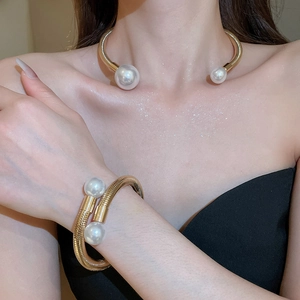 Close-up of minimalist golden pearl choker and open cuff bracelet set for women