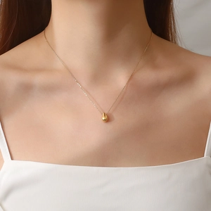 Dettaglio della collana dorata con ciondolo a goccia lucido indossata da una modella