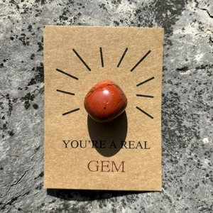 Macro view of a polished red crystal stone on a You're a Real Gem kraft paper gift card
