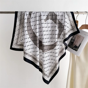 Detail of a square silk scarf with black monogram pattern on a white background