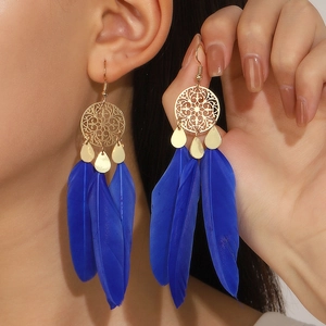 Close-up of royal blue feather earrings with golden hollow filigree on a female model