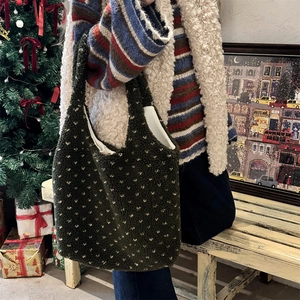 Détail d'un sac cabas en peluche vert foncé avec motifs cœurs dans un décor d'hiver