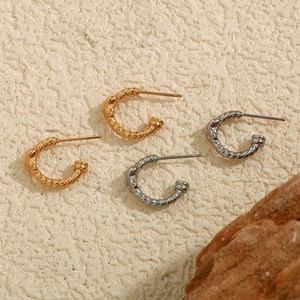 Twisted French style hoop earrings in gold and silver finish on textured background