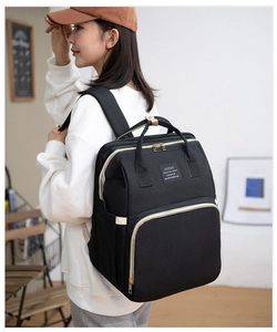 Detail of a black diaper backpack with gold zippers and beige handles on a female model