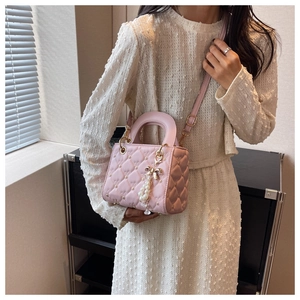 Detailed shot of pink heart-quilted handbag featuring a pearl bow charm and top handle