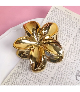 Detail of a golden flower-shaped metal hair claw clip placed on a white ceramic plate