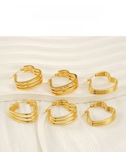 Macro view of triple-layered golden heart hoop earrings on a white display stand