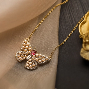 Golden butterfly necklace with red gemstone, pearls and rhinestones on silk fabric