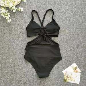Flat lay of black cut-out one-piece swimsuit with cross-back tie design and flat props