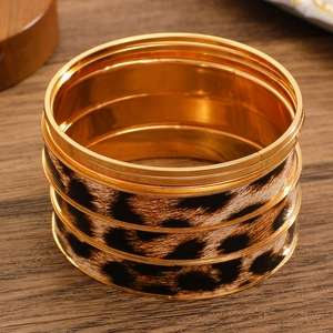 Detail of stacked gold metal bangles featuring a classic leopard print wide cuff bracelet