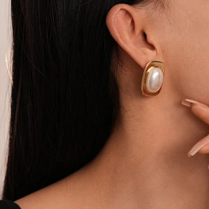 Close-up of model wearing gold square metal earrings with large oval faux pearl inlay
