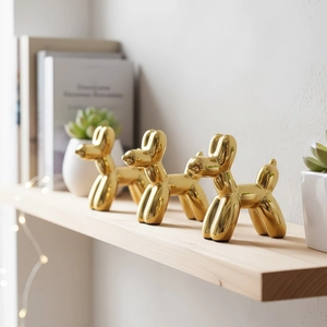 Tre statue di cane palloncino dorato con finitura a specchio su uno scaffale moderno