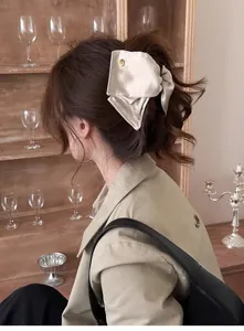 Détail de la pince à cheveux en satin crème avec logo doré dans un décor rétro chic