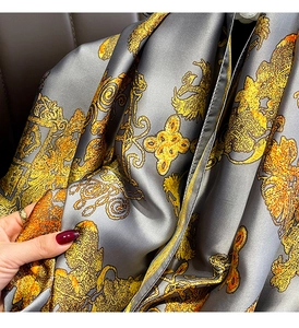 Detailed macro view of vintage gold and orange patterns on a grey silk scarf texture