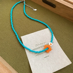 Detail of blue beaded necklace featuring an orange flower pendant and adjustable silver clasp