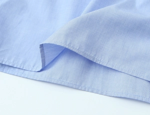 Close-up of light blue shirt hem featuring precise double-stitched rolled edge craftsmanship