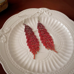 Close-up of luxury red rhinestone feather tassel earrings in a textured white ceramic dish