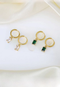 Detail of gold titanium steel hoop earrings with emerald and clear zircon square pendants