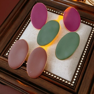 Tre paia di orecchini ovali opachi in viola, verde e rosa su un display in tessuto beige