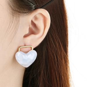 Detailed close-up of a white marble texture heart earring on a model's ear with gold trim