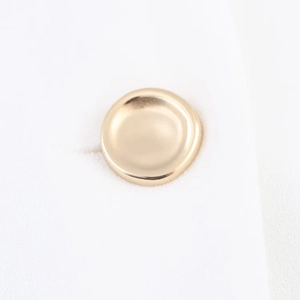 Detail of a polished round golden button sewn onto high-quality white textured fabric