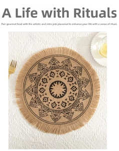 Detail of round jute placemat with black mandala pattern and fringe edge on a white tablecloth