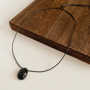 Gros plan du pendentif en obsidienne ovale poli sur cordon noir réglable et bois