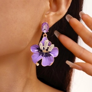 Dettaglio di orecchini a fiore in smalto viola con strass e finitura in oro lucido